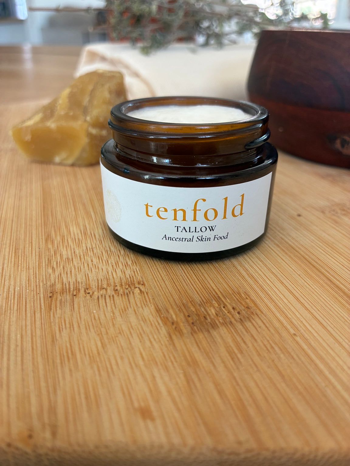 Open amber jar of Tenfold Tallow face creme on a wood surface